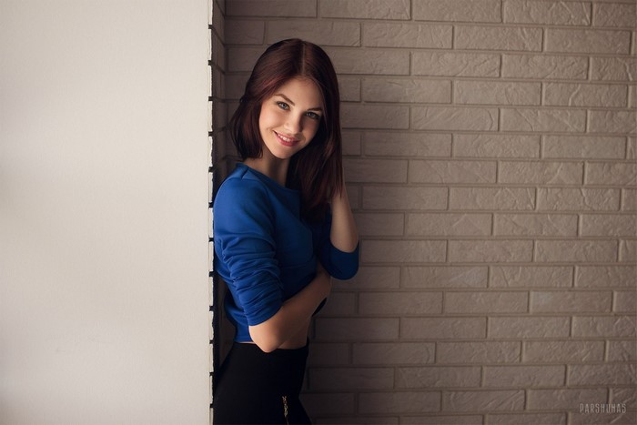 Woman in blue top and black skirt by brick wall