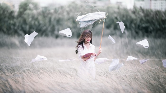 Woman in a white dress holding an umbrella in a field