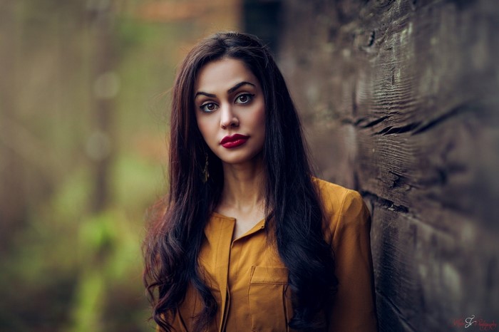 Woman with long dark hair leaning against a wooden wall