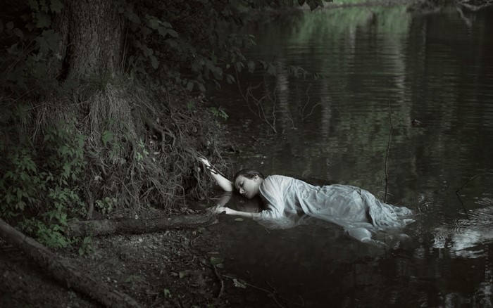 Woman lying in dark water near tree roots