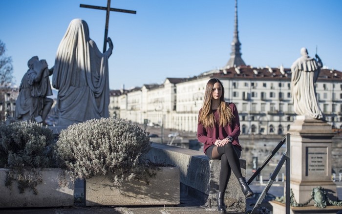 Woman sitting near statues with Mole Antonelliana in Turin