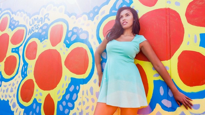 Woman in a mint green dress posing against a colorful mural