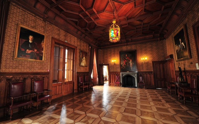 Interior of a grand wooden room with paintings and a chandelier