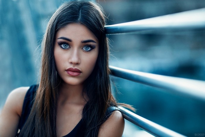 Woman with blue eyes and long brown hair leaning on railing