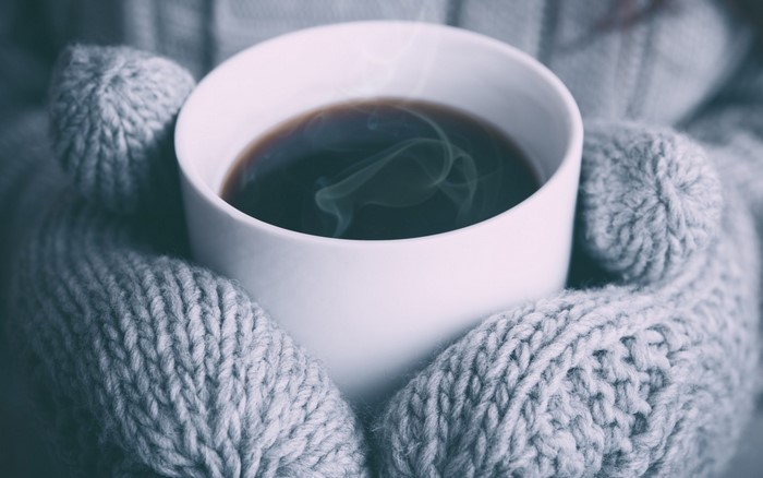 Close up of a steaming cup of coffee held by hands in knitted gloves