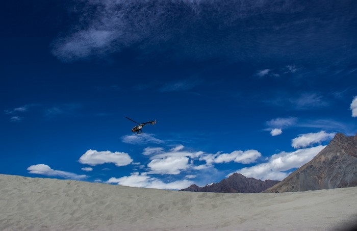 Helicopter flying over sand dunes with mountains