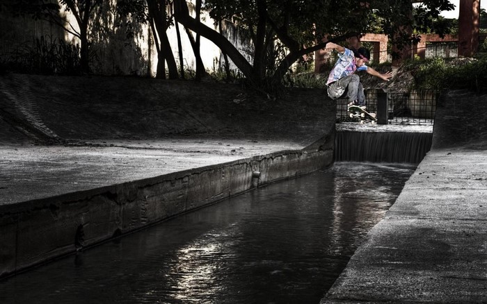 Man skateboarding over a waterfall in a canal
