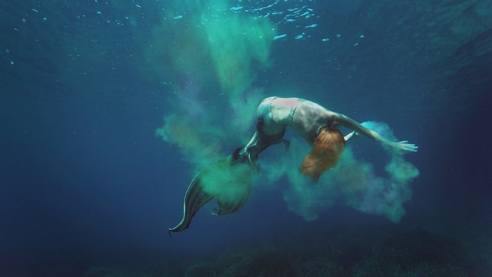 Mermaid diving underwater with green dust