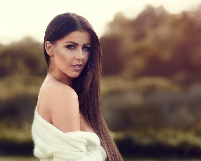 Woman with long brown hair wearing a white sweater outdoors