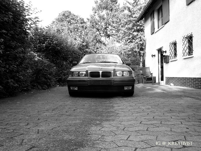 BMW E36 parked on a cobblestone driveway next to a house