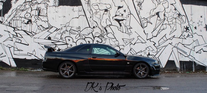 Black Nissan Skyline GT-R R34 parked in front of graffiti wall