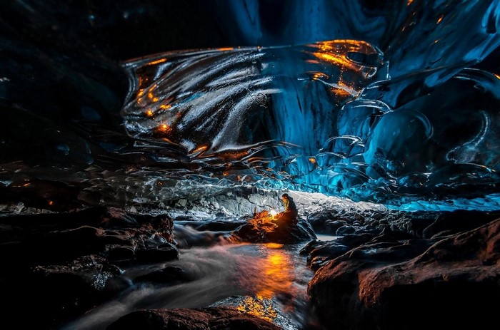 Man with lantern in Iceland ice cave with river