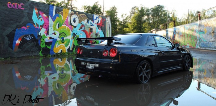 Black Nissan Skyline GT-R R34 parked by graffiti wall