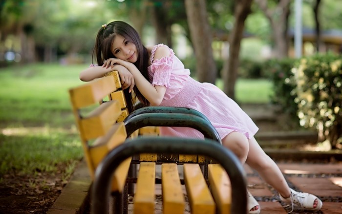 Young Asian woman in pink dress sitting on park bench