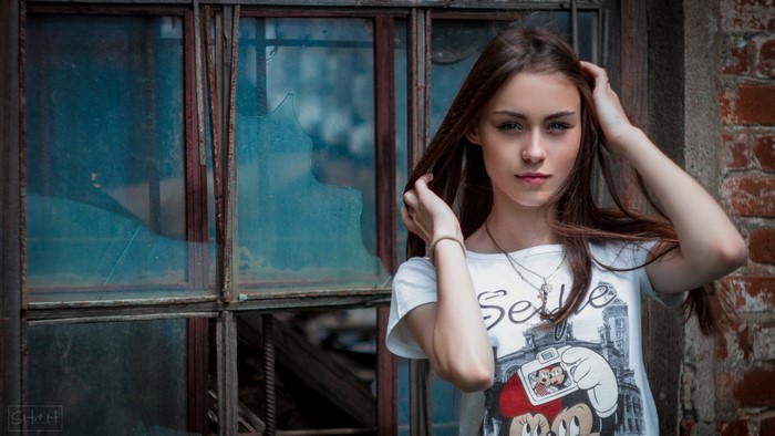 Young woman with hands in hair in front of broken window