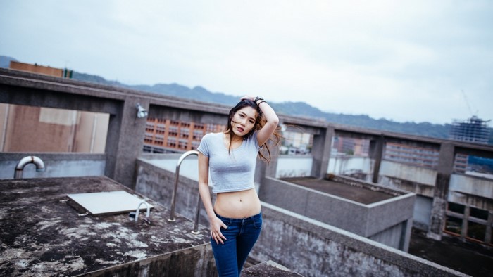 Asian woman in crop top and jeans on urban rooftop