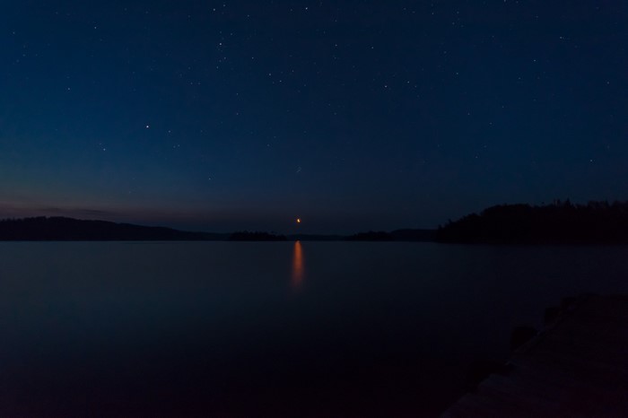 Night sky over a calm lake with stars and moon reflection