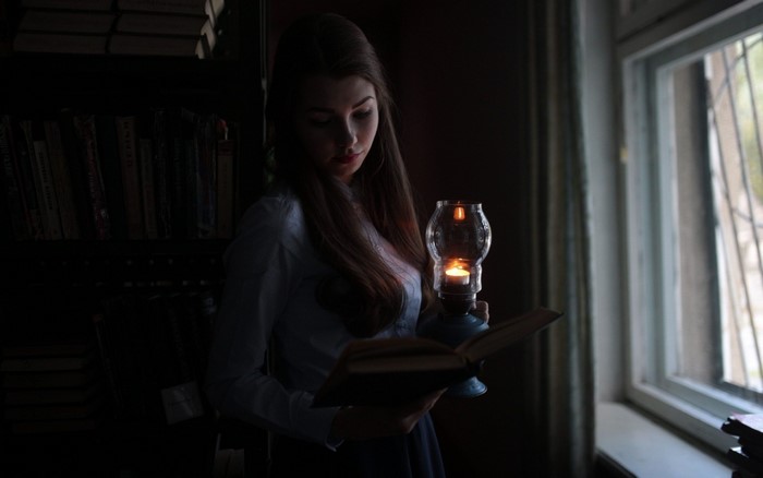 Woman reading a book by lantern light near a window