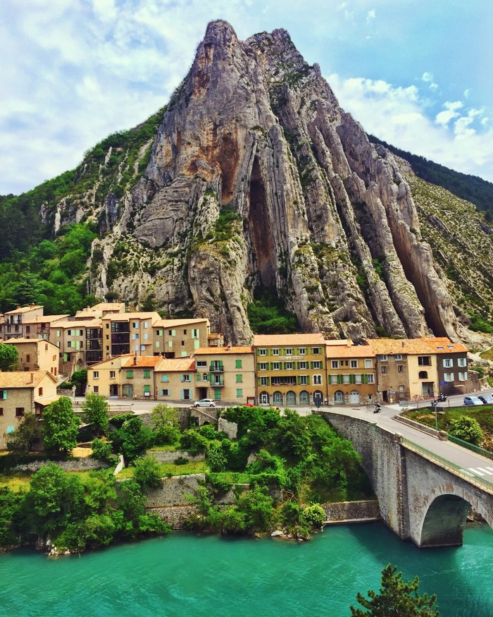 Village nestled below a dramatic mountain by a turquoise river in France