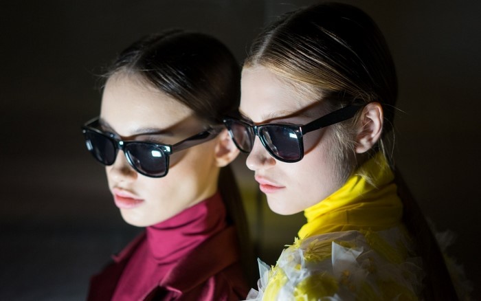 Two models wearing sunglasses and fashionable outfits