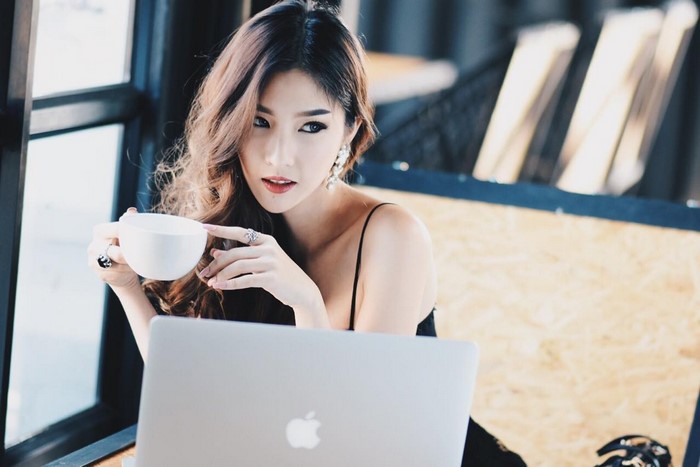 Asian woman holding coffee cup in front of laptop