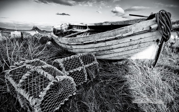 Abandoned boat and lobster pots on grassy shore with castle in distance