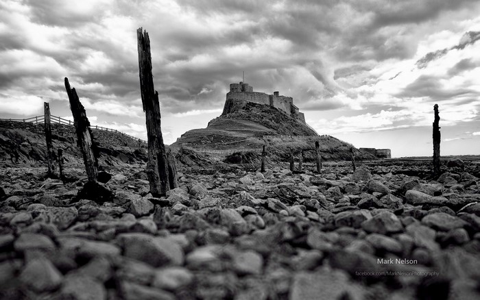 Lindisfarne Castle on a rocky shore with wooden posts