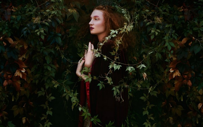Woman with red hair in a dark forest surrounded by vines