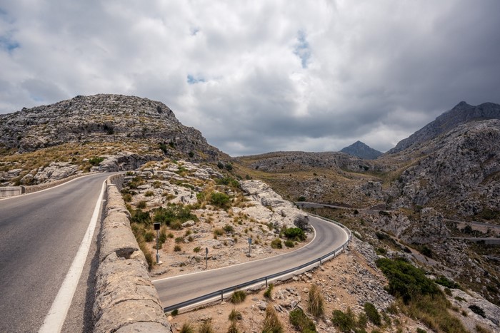 Winding mountain road through rocky terrain under cloudy sky