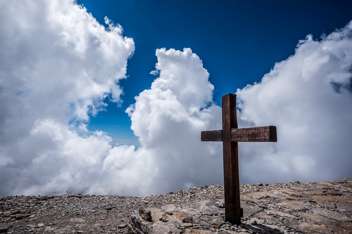 Wooden cross on a rocky mountain peak with clouds