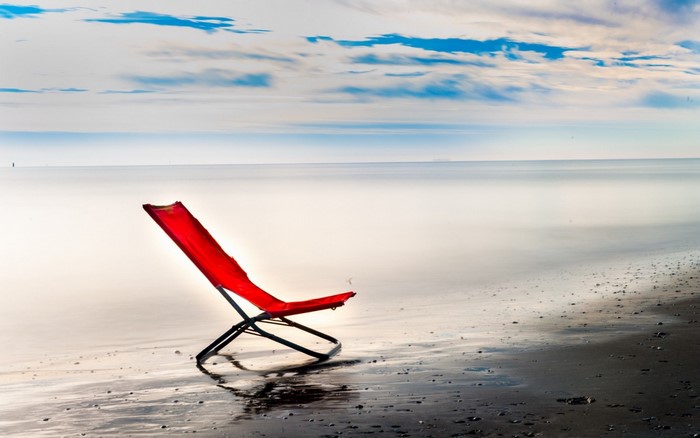 Red chair on a beach with ocean and clouds