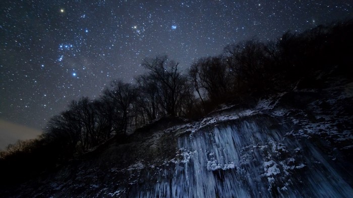 Winter night sky with stars over icy cliff