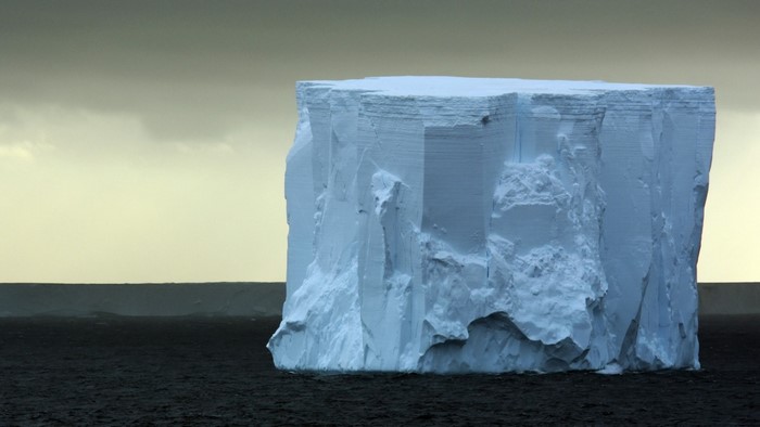 A large tabular iceberg in dark water under a cloudy sky