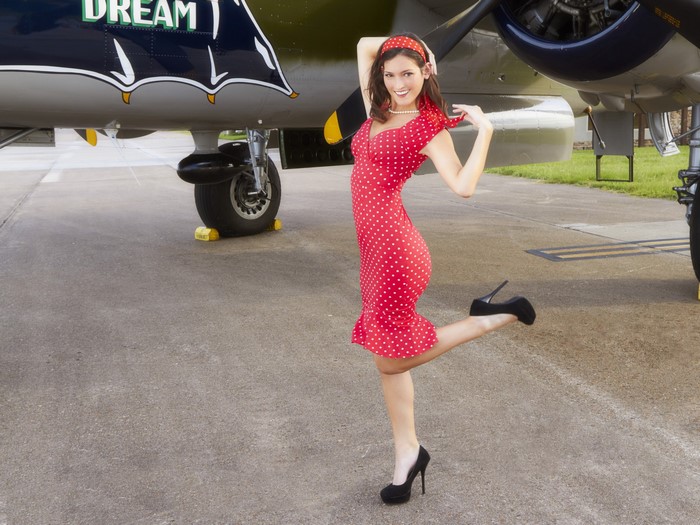 Woman in red polka dot dress posing by airplane
