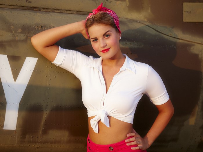 Woman in white shirt and pink skirt posing against a wall