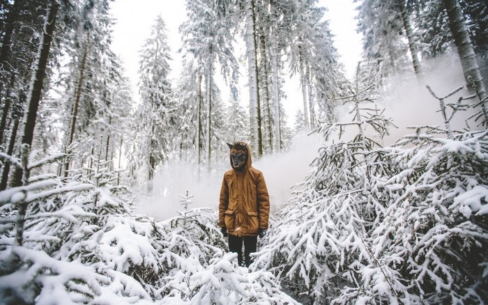 Person in wolf mask in snowy forest with smoke