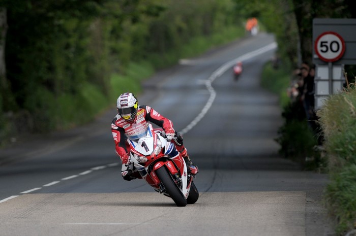Motorcyclist racing on a road with trees and a speed limit sign