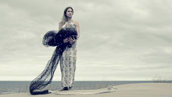 Woman in a patterned dress holding a black net on a beach