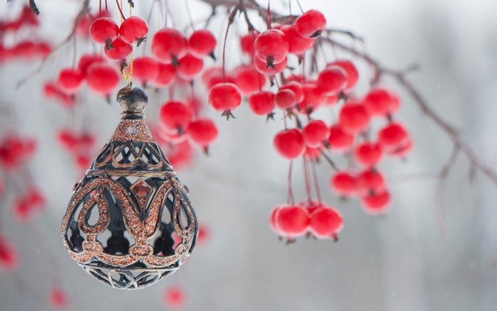 Ornate Christmas ornament hanging from a branch with red berries