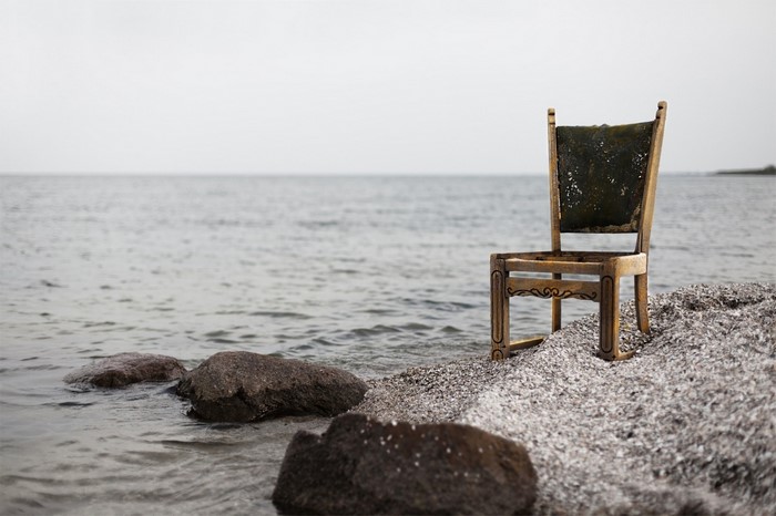 An old wooden chair on a rocky shore by the sea