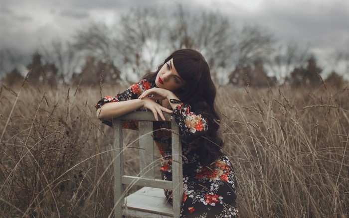Woman in floral dress sitting on a chair in a field