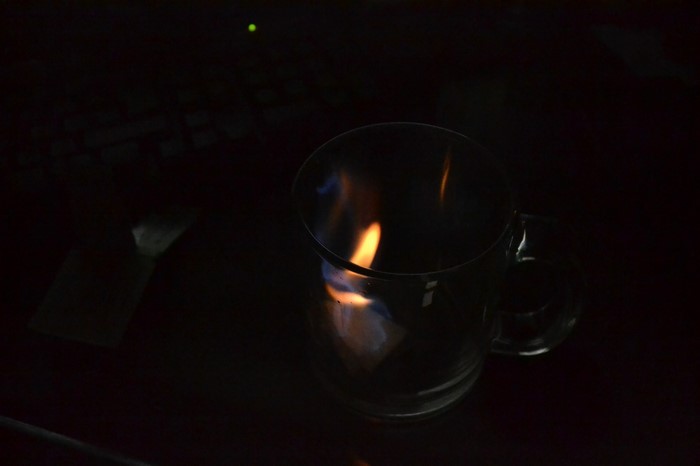 Fire burning inside a glass mug on a dark surface