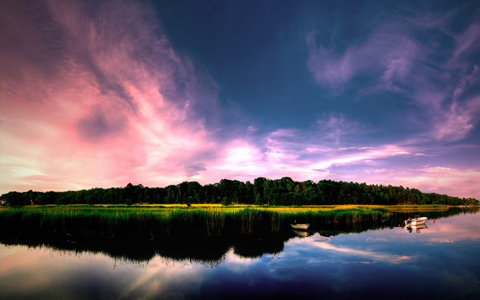 Panoramic sunset over a lake with trees and boats