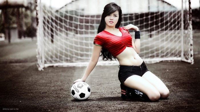 Asian woman in red top and black shorts with soccer ball