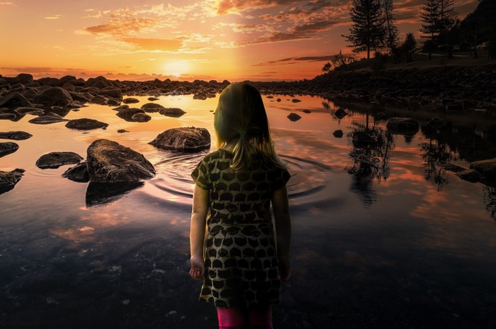 Girl watching sunset over rocky ocean landscape