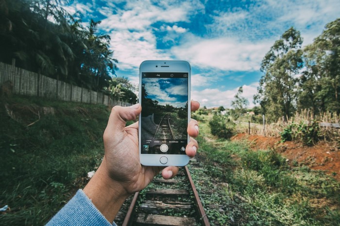 Hand holding iPhone taking picture of railway tracks