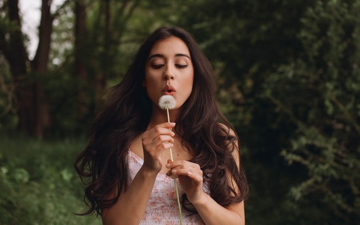 Woman blowing dandelion in a forest