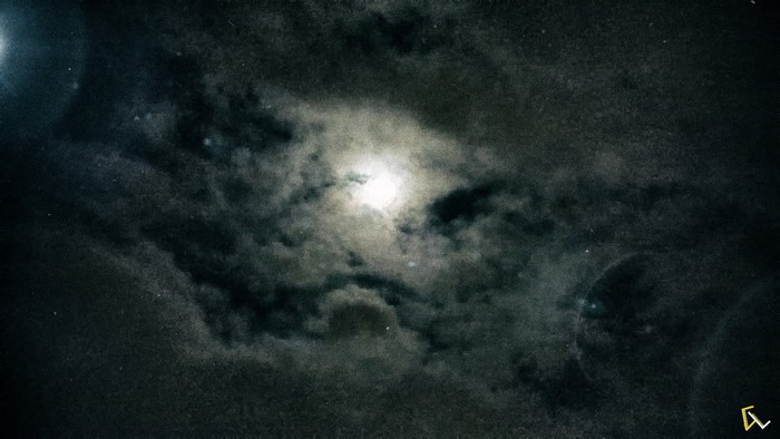 Moonlight through dark clouds in the night sky
