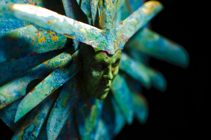 Close up of a green and blue metallic sculpture with a face