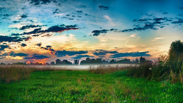 Misty field at sunrise with colorful clouds